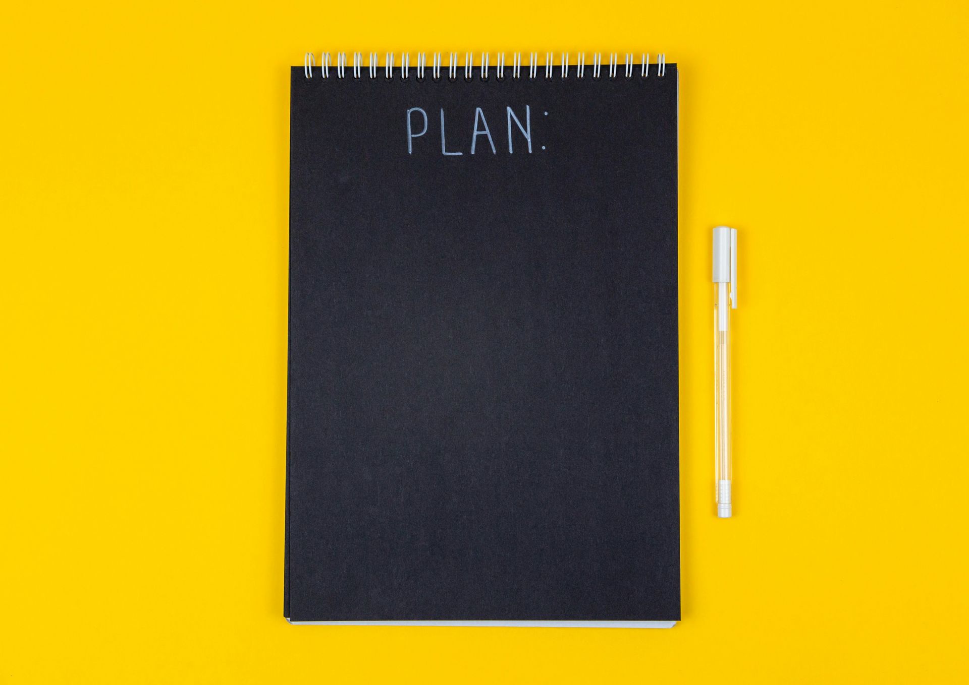 Een notitieblok met het woord PLAN erop, met pen, op een gele ondergrond