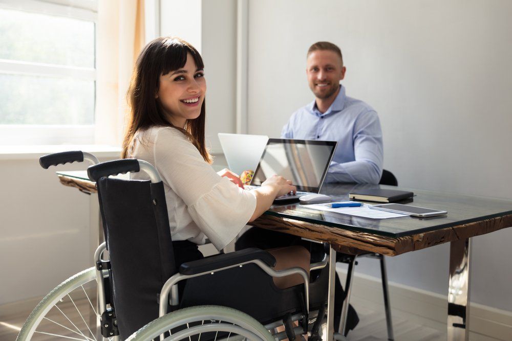Een vrouw in een rolstoel werkt samen met een collega aan een tafel met laptops