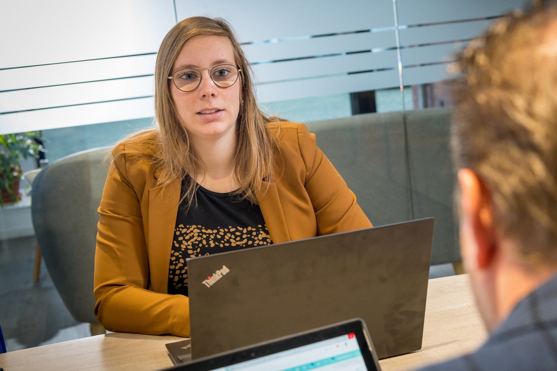Een medewerker in gesprek achter haar laptop aan een overlegtafel
