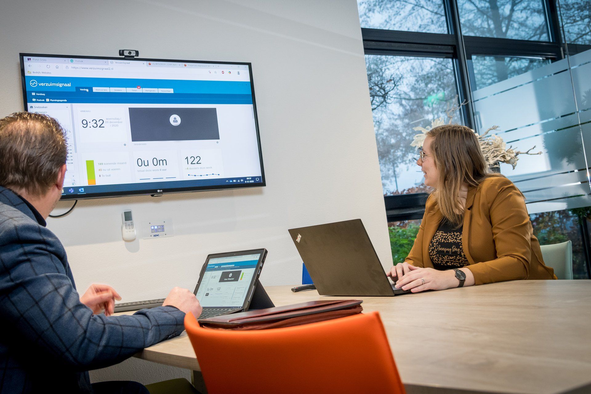 Twee medewerkers achter hun laptop in een overlegruimte met een groot scherm