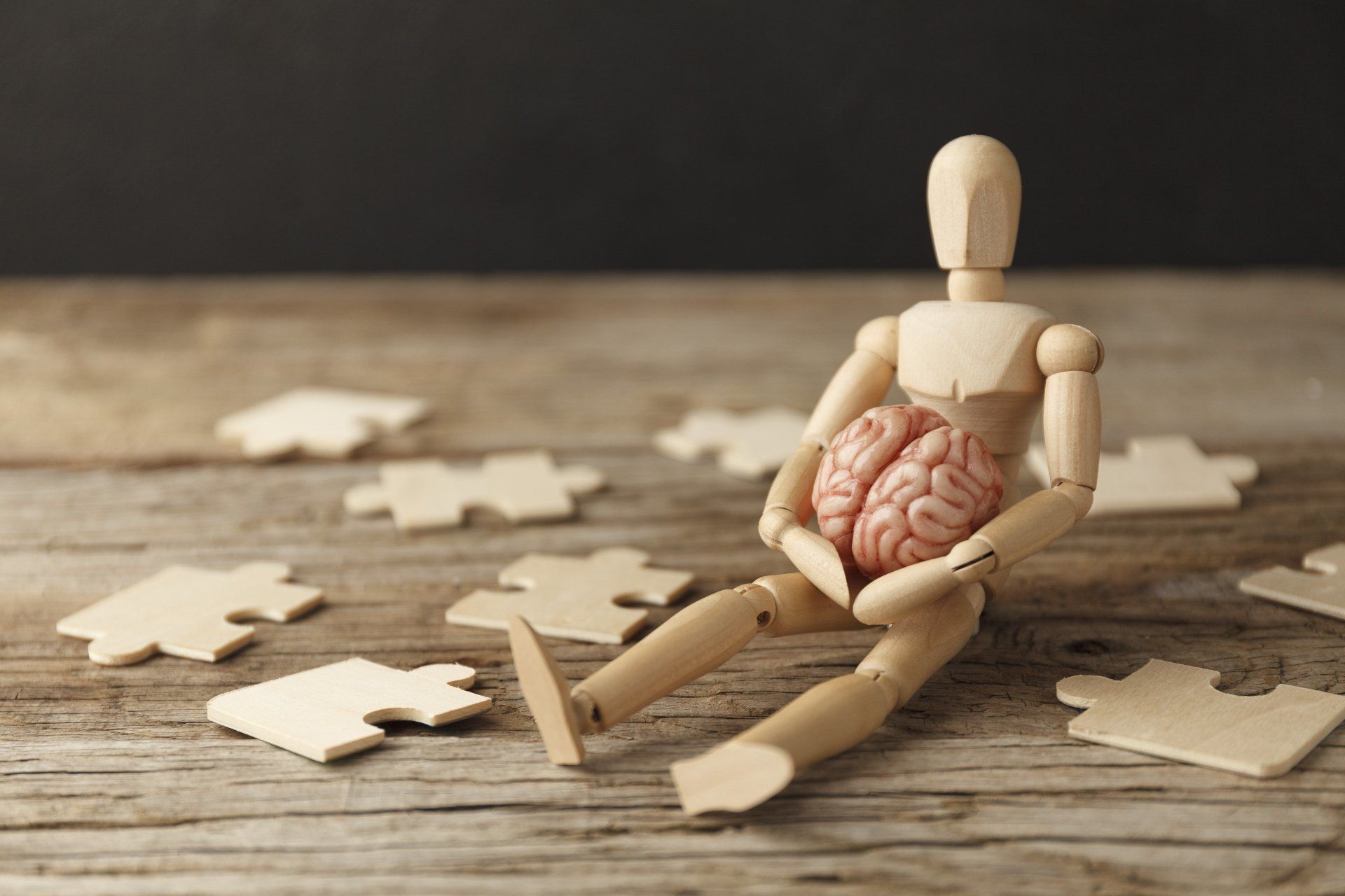 Een houten ledenpop tussen puzzelstukjes, met een puzzelstuk in de vorm van hersenen