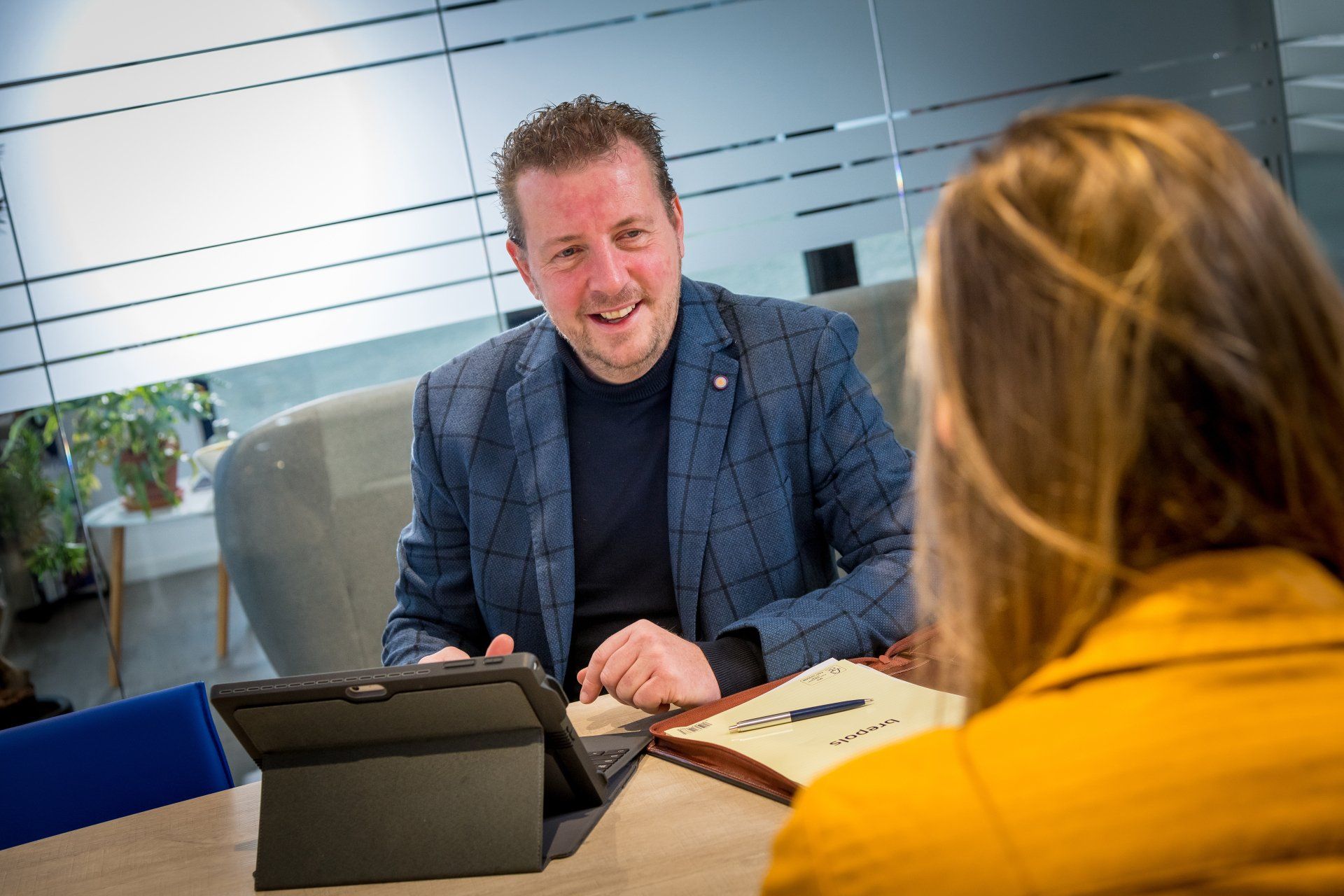 Twee mensen bespreken papieren en een tablet aan een overlegtafel