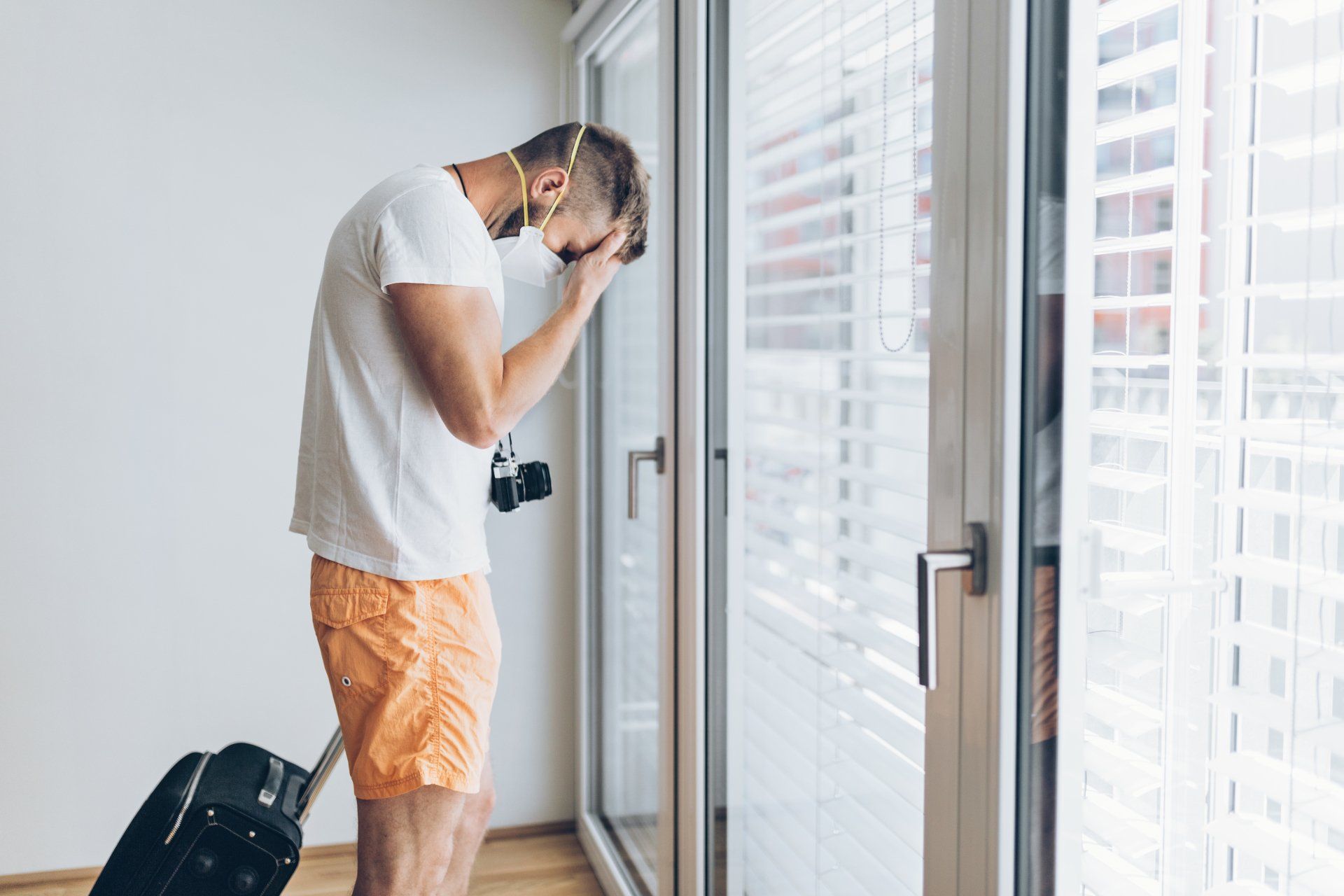 Een man met een koffer staat verslagen bij het raam van een hotelkamer
