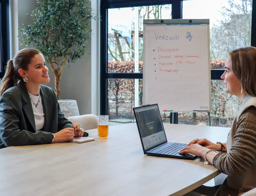 Twee collega&rsquo;s nemen aan tafel een dossier door, met aantekeningen en een laptop